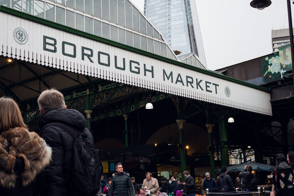 The image depicts a busy outdoor market scene under a canopy, with multiple green and yellow striped umbrellas displaying the sign 'BOURGH MARKET' in bold white letters. Several stalls are visible, wi